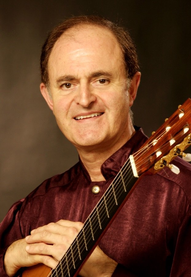 Julian Byzantine in a burgundy shirt, resting his hands on his guitar
