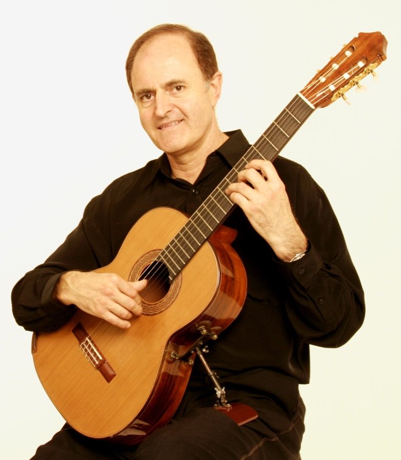 Julian Byzantine seated with his guitar, smiling, against a white background